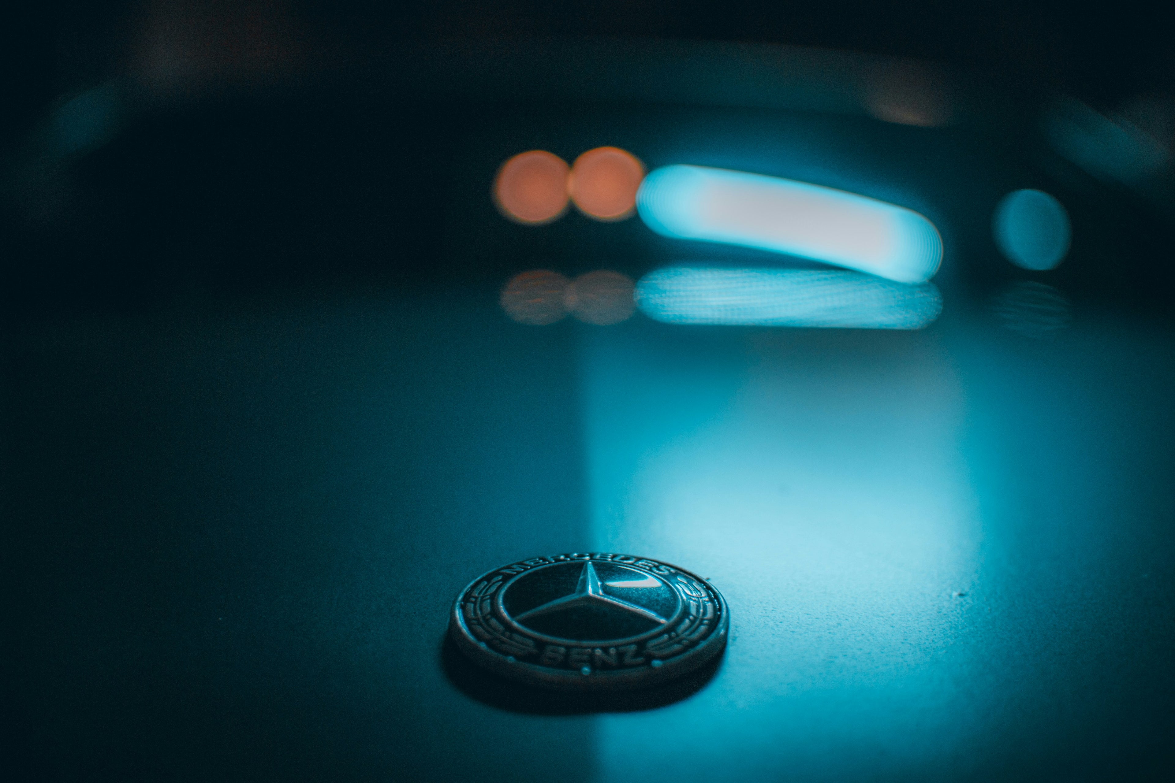 Close-up of an Illuminated Mercedes-Benz emblem on the hood of a car at night, symbolizing luxury and performance.