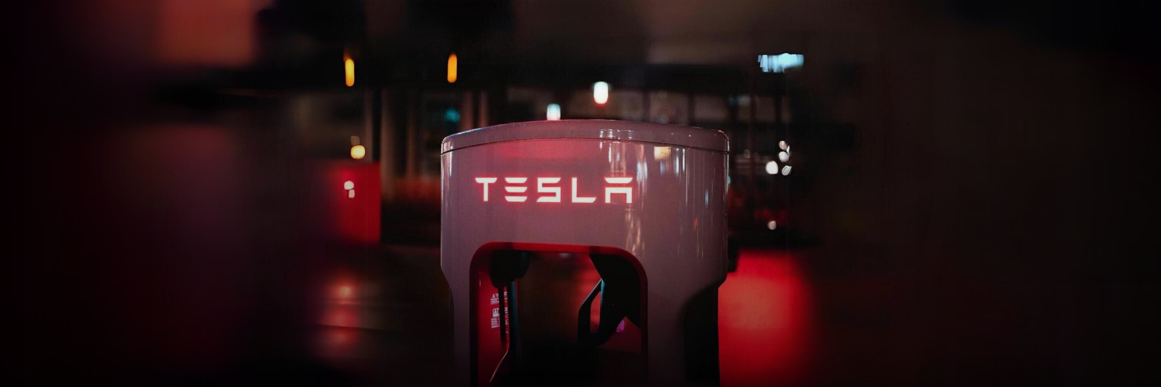 Illuminated red and orange hues Tesla charging station with soft ambient lighting in the background in a dimly lit environment, providing power to Tesla models..