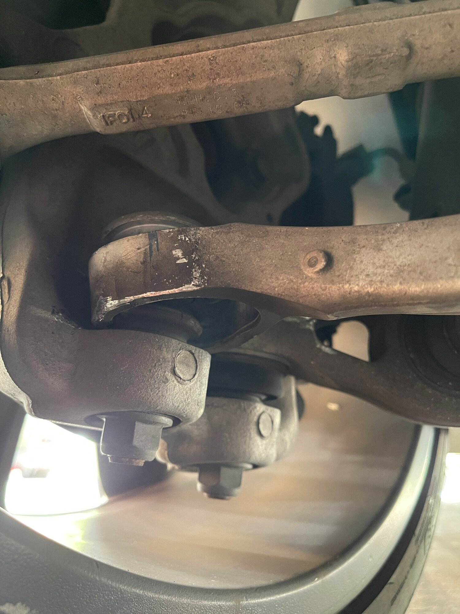 A close-up of a car suspension system showing a broken lower control arm on a Tesla Model S. The control arm is a metal component that connects the wheel to the car's frame and is critical for safe driving. In the image, the control arm is cracked near the wheel hub.